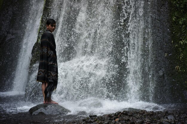 Foto met een lombok-indonesiese songket-doek aan en genietend van de frisheid van een waterval