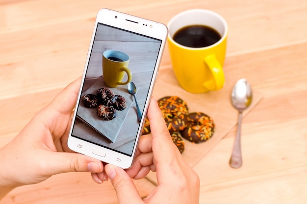 Met een mobiele telefoon hete koffie en koekjes op een houten achtergrond fotograferen