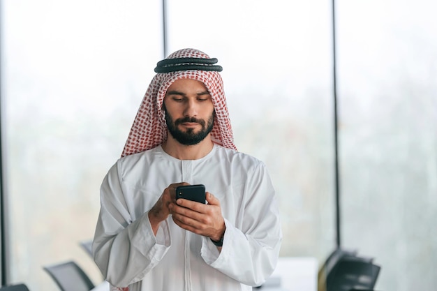 Met een smartphone in de hand een succesvolle moslim zakenman in traditionele kleding in zijn kantoor