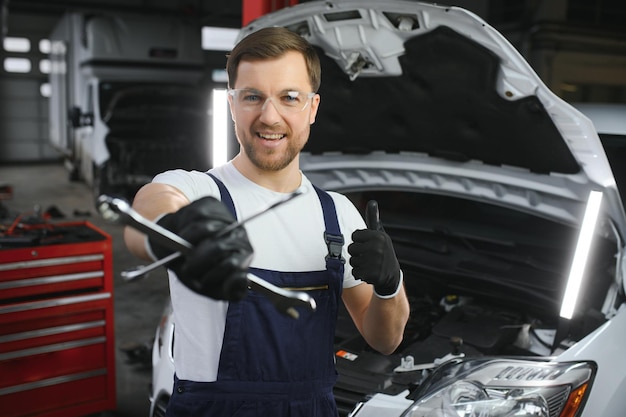 Met gereedschap in de hand Volwassen man in gekleurd uniform werkt in de autosalon