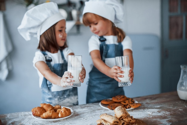 Met glazen met melk. Familie kinderen in witte chef-kok uniform bereiden van voedsel in de keuken.