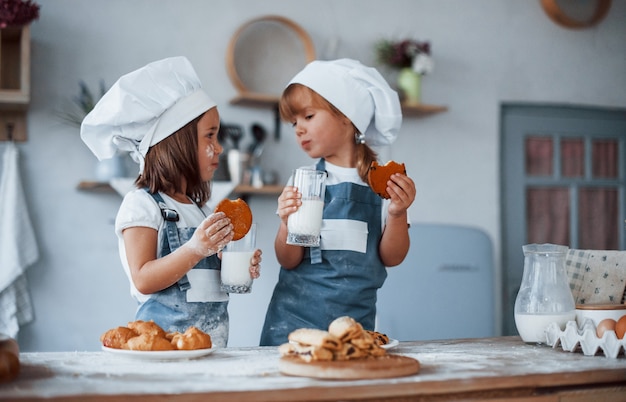 Met glazen met melk. Familie kinderen in witte chef-kok uniform bereiden van voedsel in de keuken.
