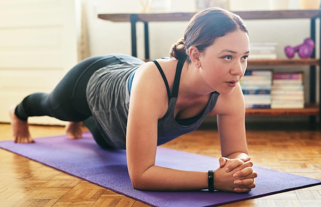 Foto met het einddoel voor ogen bijgesneden opname van een aantrekkelijke jonge vrouw die yoga doet en een plank poseert in haar huis