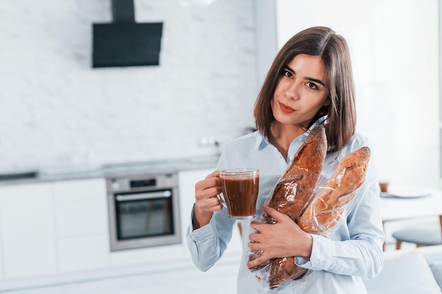 Met kopje koffie jonge vrouw is overdag binnenshuis in de kamer van een modern huis