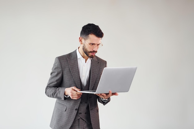 Met laptop in handen Jonge stijlvolle zakenman in pak binnenshuis Conceptie van succes