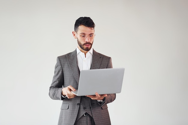 Met laptop in handen Jonge stijlvolle zakenman in pak binnenshuis Conceptie van succes