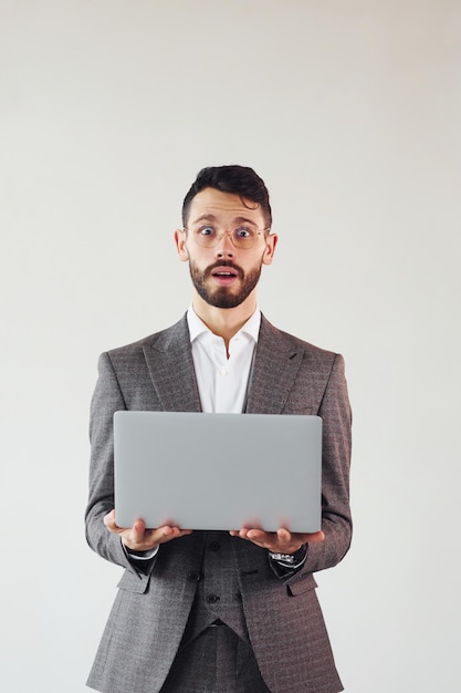 Met laptop in handen Jonge stijlvolle zakenman in pak binnenshuis Conceptie van succes