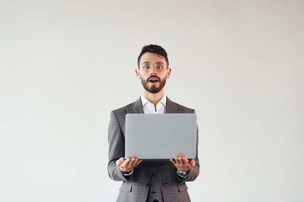 Met laptop in handen Jonge stijlvolle zakenman in pak binnenshuis Conceptie van succes