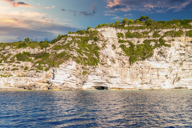 Met planten bedekte hoge rotswanden aan de kust van het eiland Corfu in Griekenland met helder turkoois zeewater onder blauwe wolkenloze hemelpanorama