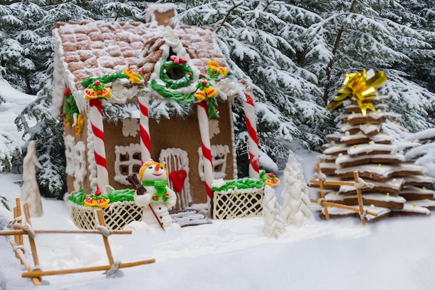 Met sneeuw bedekte zelfgemaakte peperkoek huis, peperkoek kerstboom en een suiker mastiek sneeuwpop op bos achtergrond. Mockup voor seizoensaanbiedingen en kerstkaart