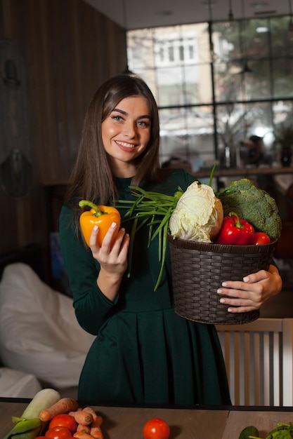 Met veel groenten in de mand staat mooie vrouw en neemt een peper