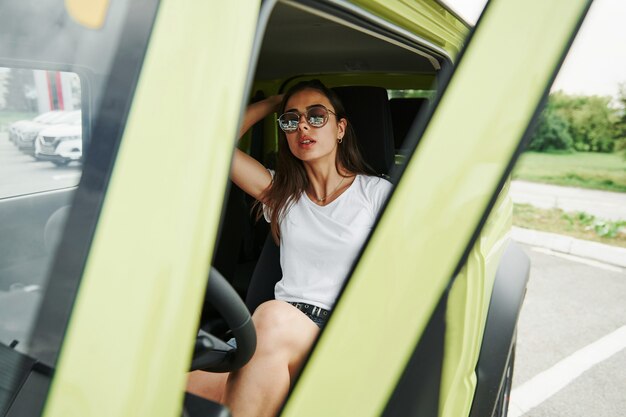 Met zonnebril. mooie vrouw in de groene moderne auto poseren