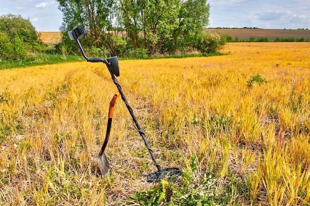 Metaaldetector en schop voor het zoeken naar munten en edele metalen tegen de achtergrond van geel veld en groen bos