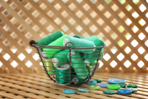 Metal basket with green sewing threads and buttons on wooden grating