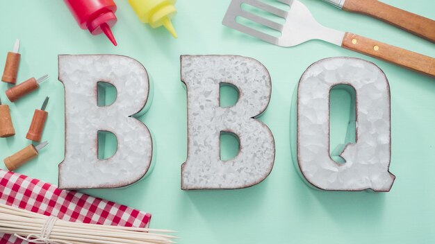 Metal BBQ sign with grilling tools on blue background.