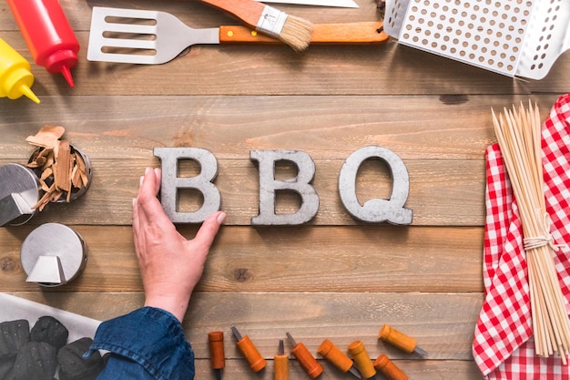 Metal BBQ sign with grilling tools on wood background.