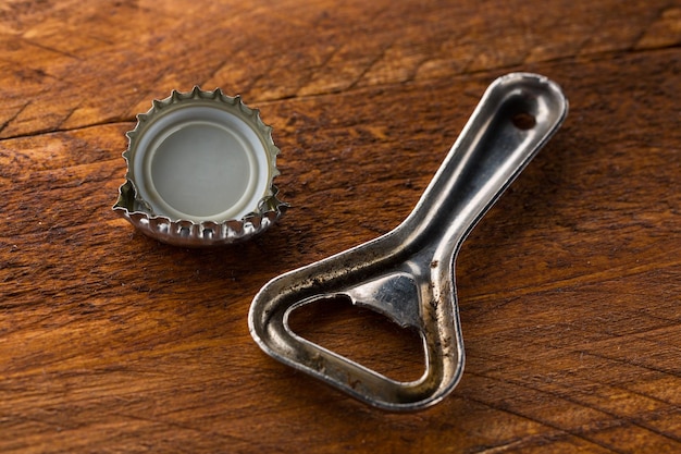 A metal bottle opener with bottle caps on wooden background.\
taken in studio with a 5d mark iii.