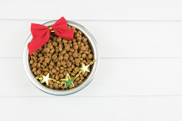 Photo metal bowl with dry pet food and christmas decorations on light boards. christmas pet supplies concept