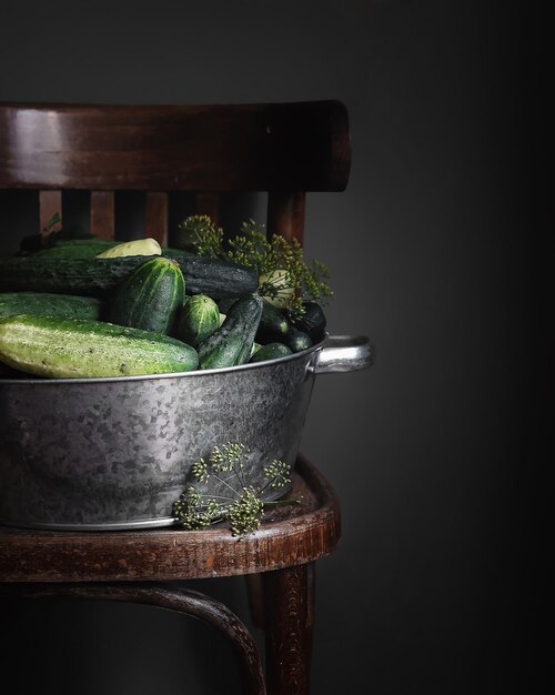 metal bowl with fresh cucumbers and dill on dark gray background