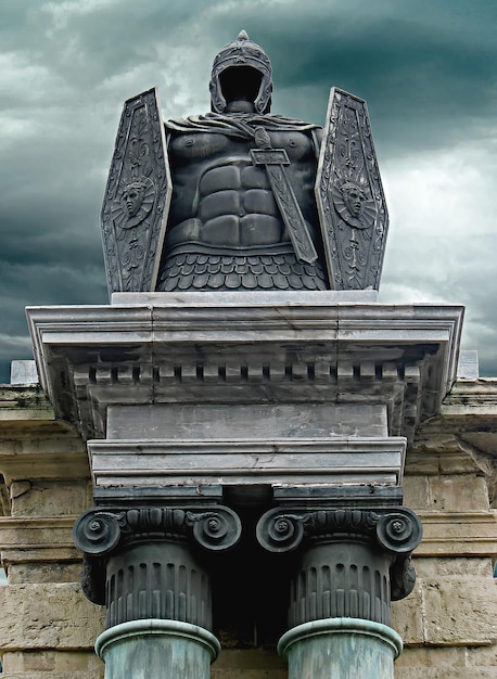 металлический бронзовый памятник воину на древней колонне на фоне драматического неба