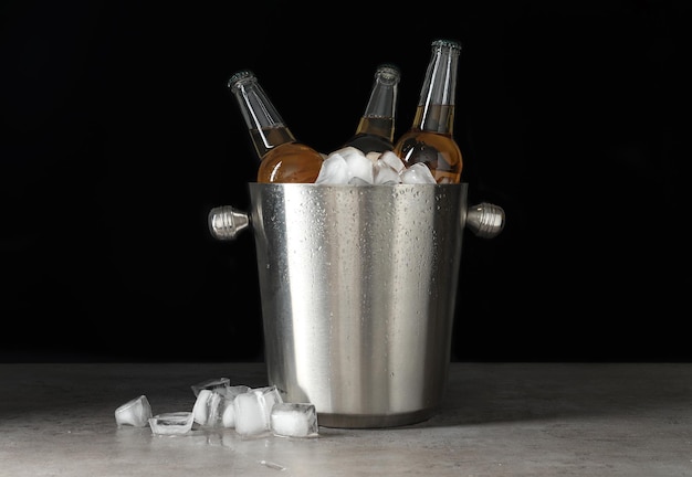 Metal bucket with bottles of beer and ice cubes on grey table