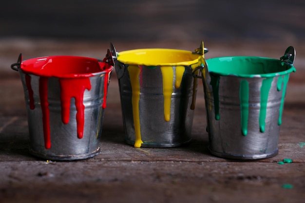 Metal buckets with colorful paint on wooden background