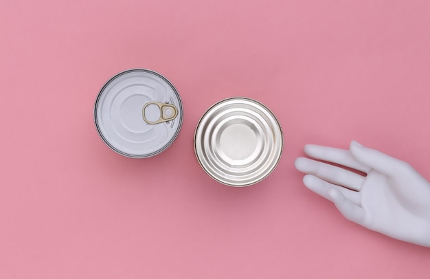 Metal cans of canned food and mannequin hand on pink background. Minimalism. Top view