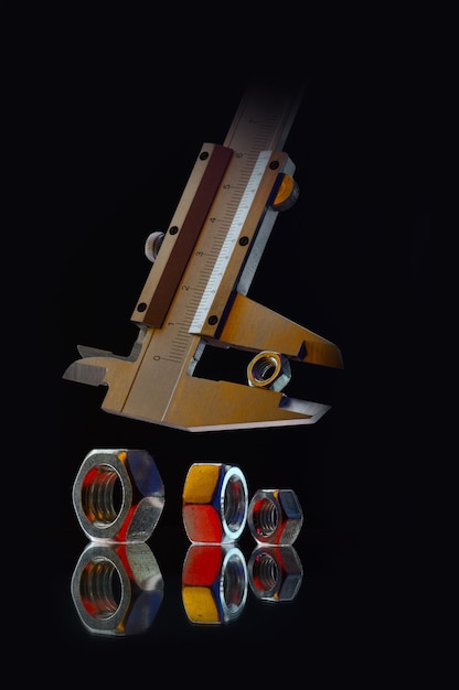 Фото Металлические хромированные гайки разных размеров и штангенциркуль для измерения гайки черный фон