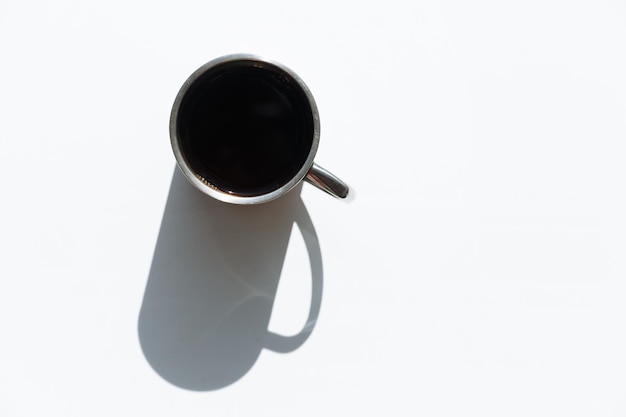 Metal cup with black coffee inside with a big shadow on the white isolated table