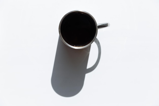Tazza di metallo con caffè nero all'interno con una grande ombra sul tavolo bianco isolato
