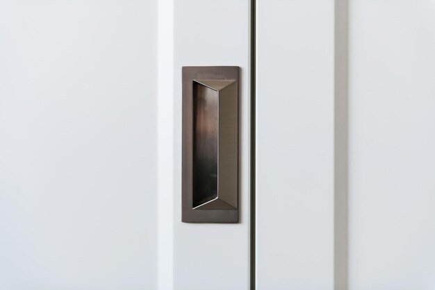 Metal dark handle in a white wooden cabinet door