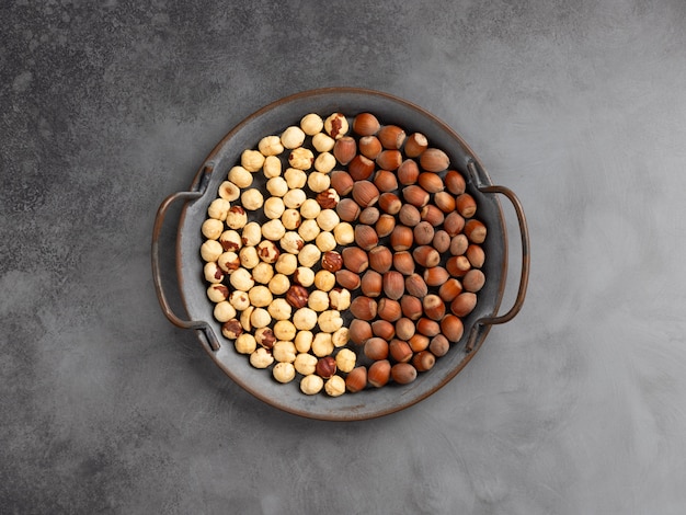 Metal dish with hazelnut kernels and whole hazelnuts in shell on a gray concrete wall. vegetarian food concept.