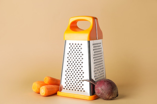 Metal grater, carrots and beetroot on color background