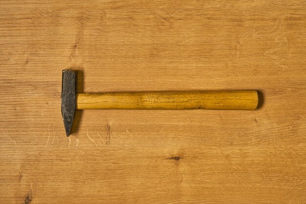 A metal hammer with a wooden handle on a wooden surface.