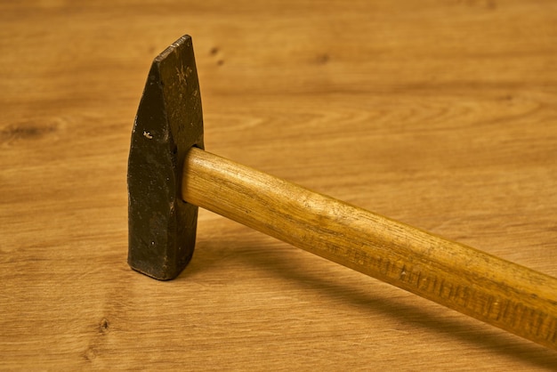 A metal hammer with a wooden handle on a wooden surface.