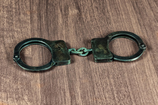 Metal handcuffs lie on a wooden table