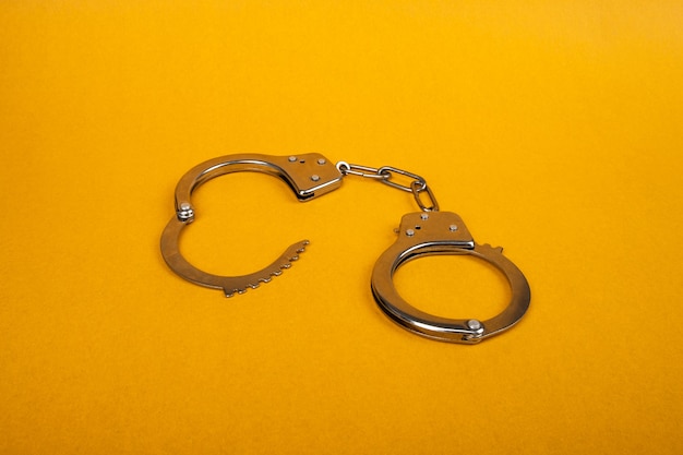 Metal handcuffs on a yellow background, concept of arrest.