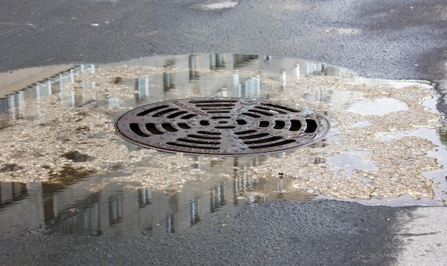 Металлический люк, слив, слив, вода возле люка на улице