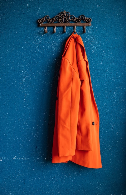 Photo metal hooks on the background of a blue wall. a red women's jacket is hanging on a hanger.plaster on the wall. rough, uneven surface. vintage background and texture.