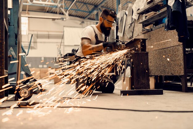 A metal industry worker processing metal parts with grinder at workshop