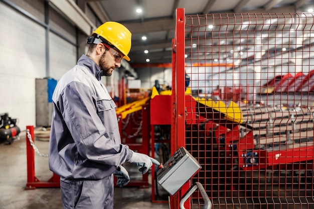 A metal industry worker using console for operating machine in factory