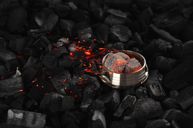 Metal kalaud with coconut charcoal cubes and sparks on a black background