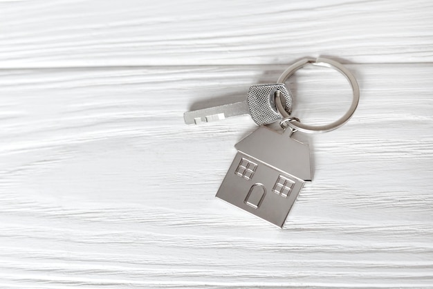 Metal keychain in the form of a house on a white wooden background, close-up.