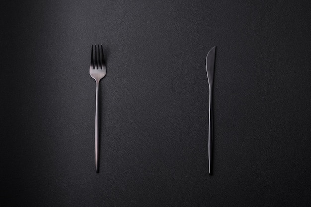 Metal kitchen knife and fork on a dark textured concrete background