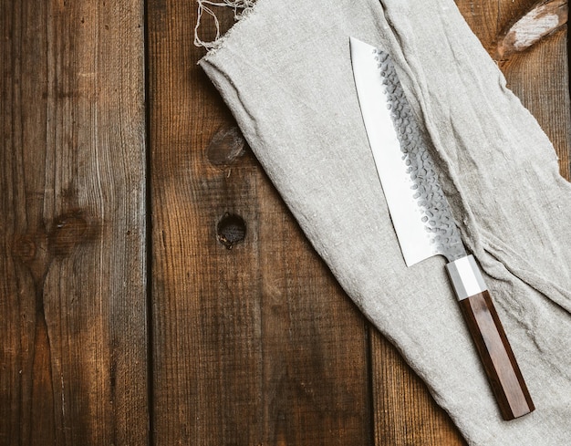 Foto coltello da cucina in metallo e tovagliolo grigio su un tavolo fatto di tavole di legno marrone vista dall'alto