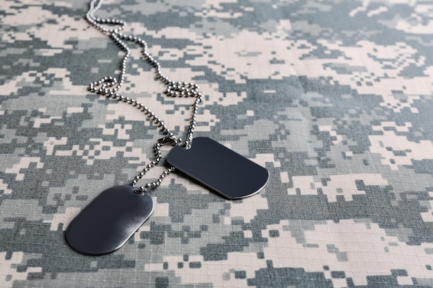 Metal military ID tags on camouflage background Space for text