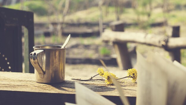 Tazza di metallo, ramo fiorito e un libro su un tavolo di legno in giardino