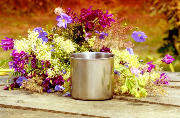 La tazza di metallo si trova sul tavolo di legno accanto a lei posare un bouquet