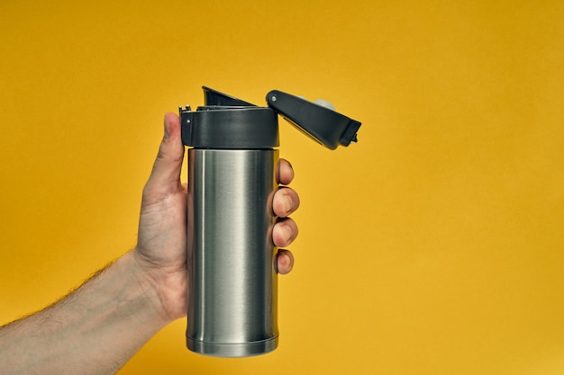 Metal mug thermos in hand on yellow