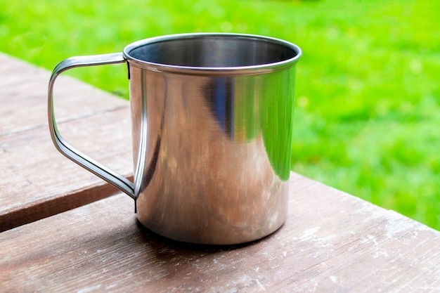 Tazza in metallo con tè o caffè sulla tavola di legno. primo piano della tazza di viaggio in campeggio con lo spazio della copia.